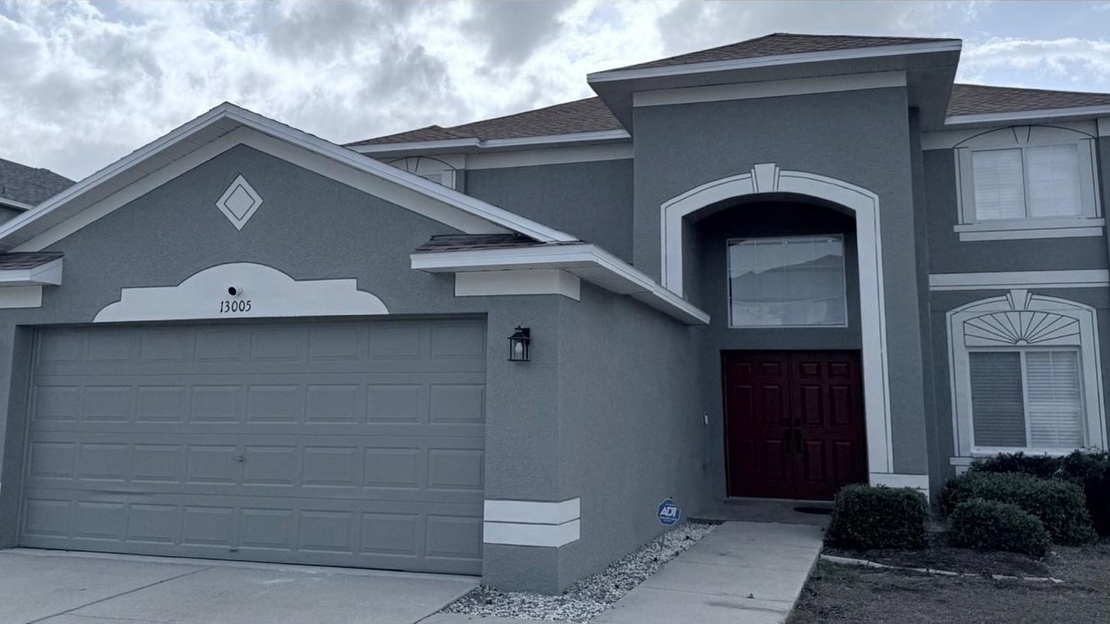 The same home after painting, deep grey stucco with white trim and a burgundy front door