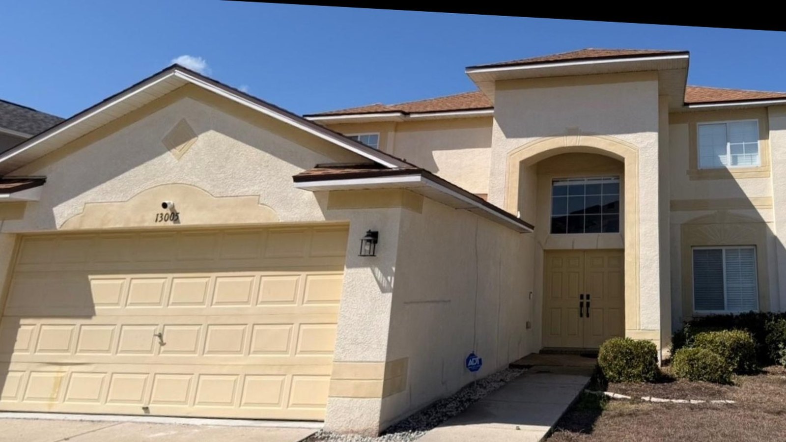 Two story Florida stucco home before painting, faded cream with a yellow garage door